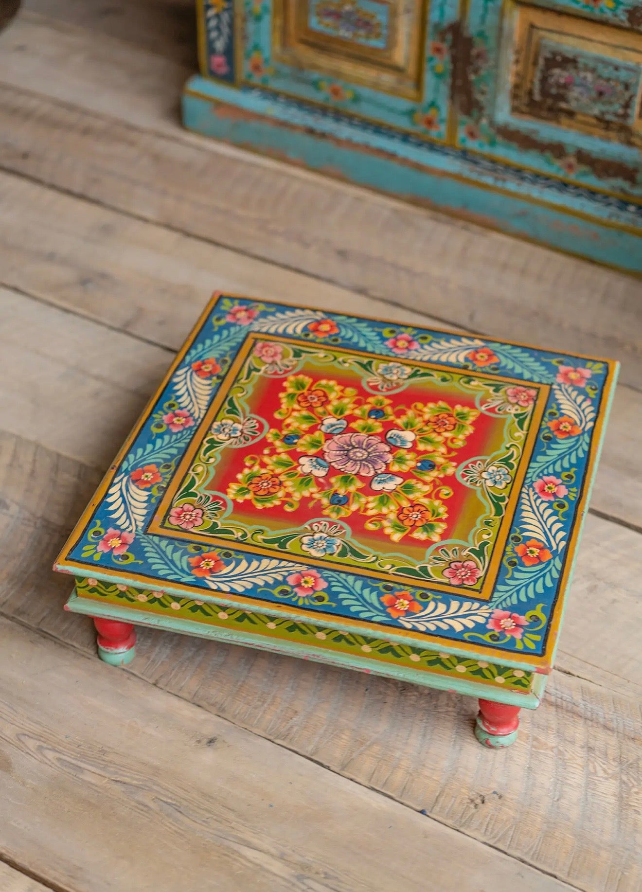 Angled view of colourful hand-painted low square table with floral pattern and turned feet