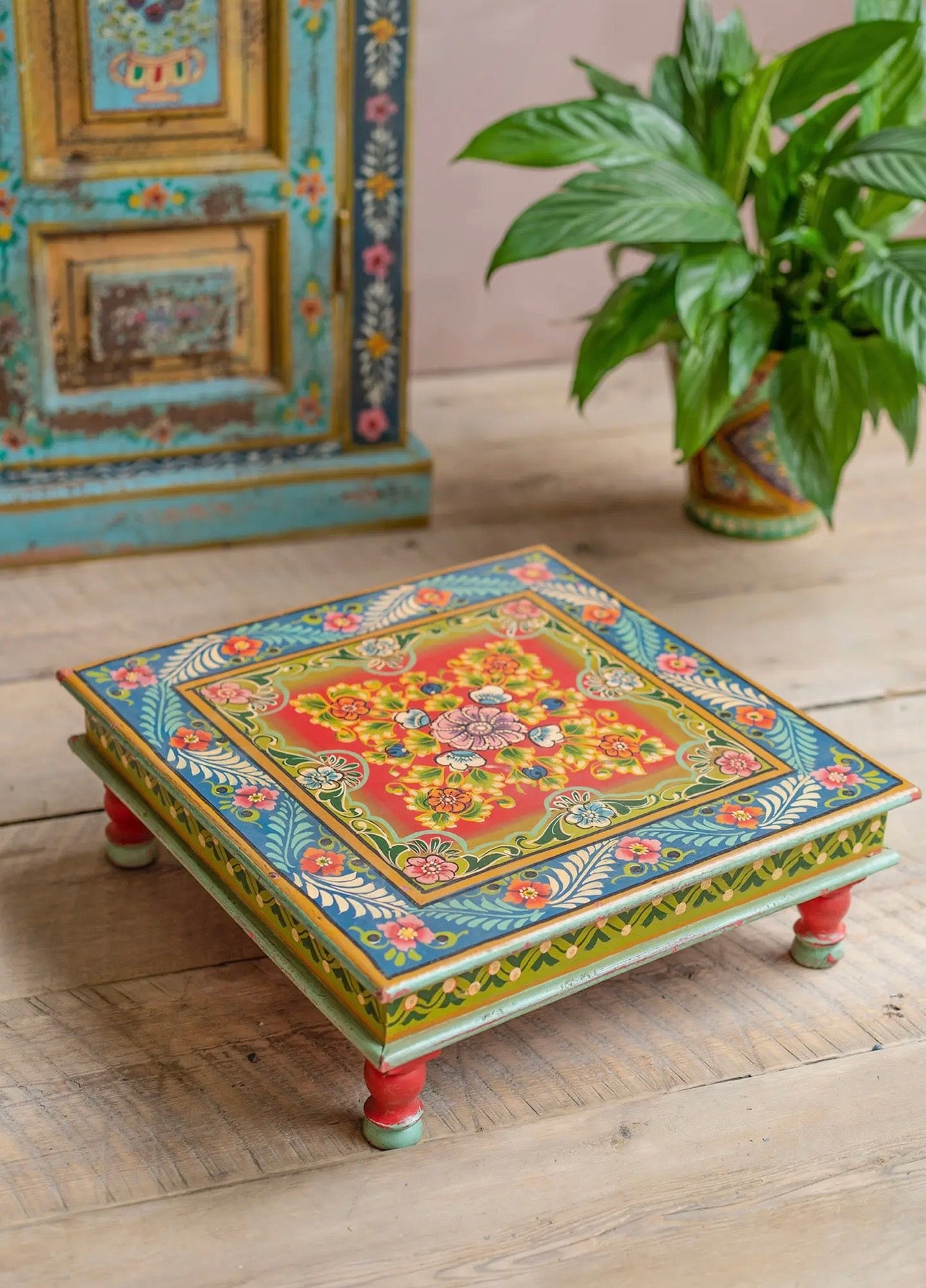 Colourful hand-painted low chowki table styled beside a plant in a vintage-inspired interior