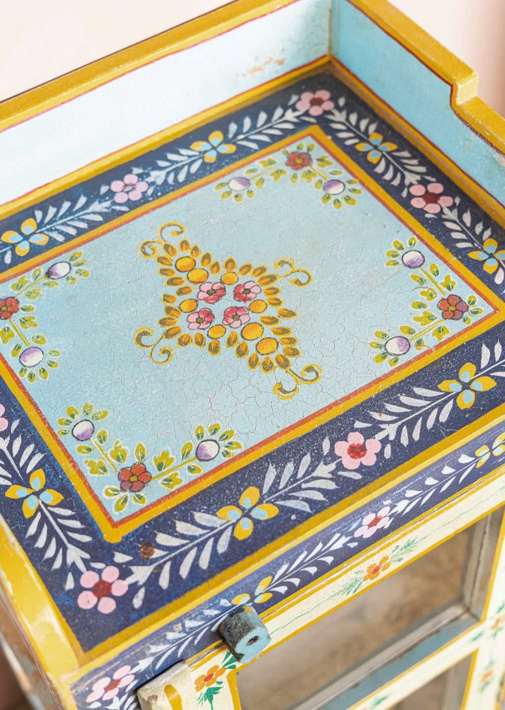 Close-up of the floral top and distressed hand-painted finish on The Neelam Display Cabinet
