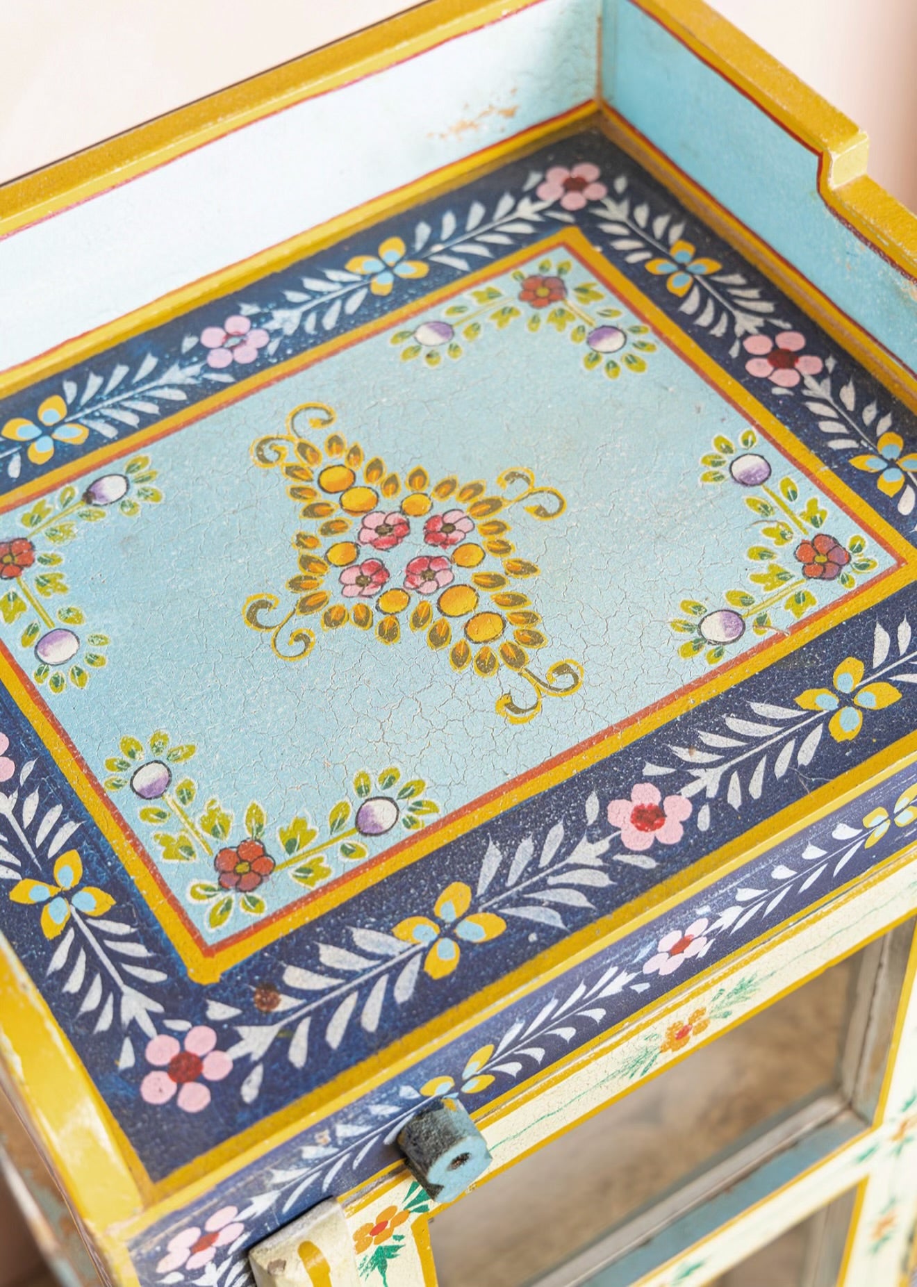 Close-up of the floral top and distressed hand-painted finish on The Neelam Display Cabinet