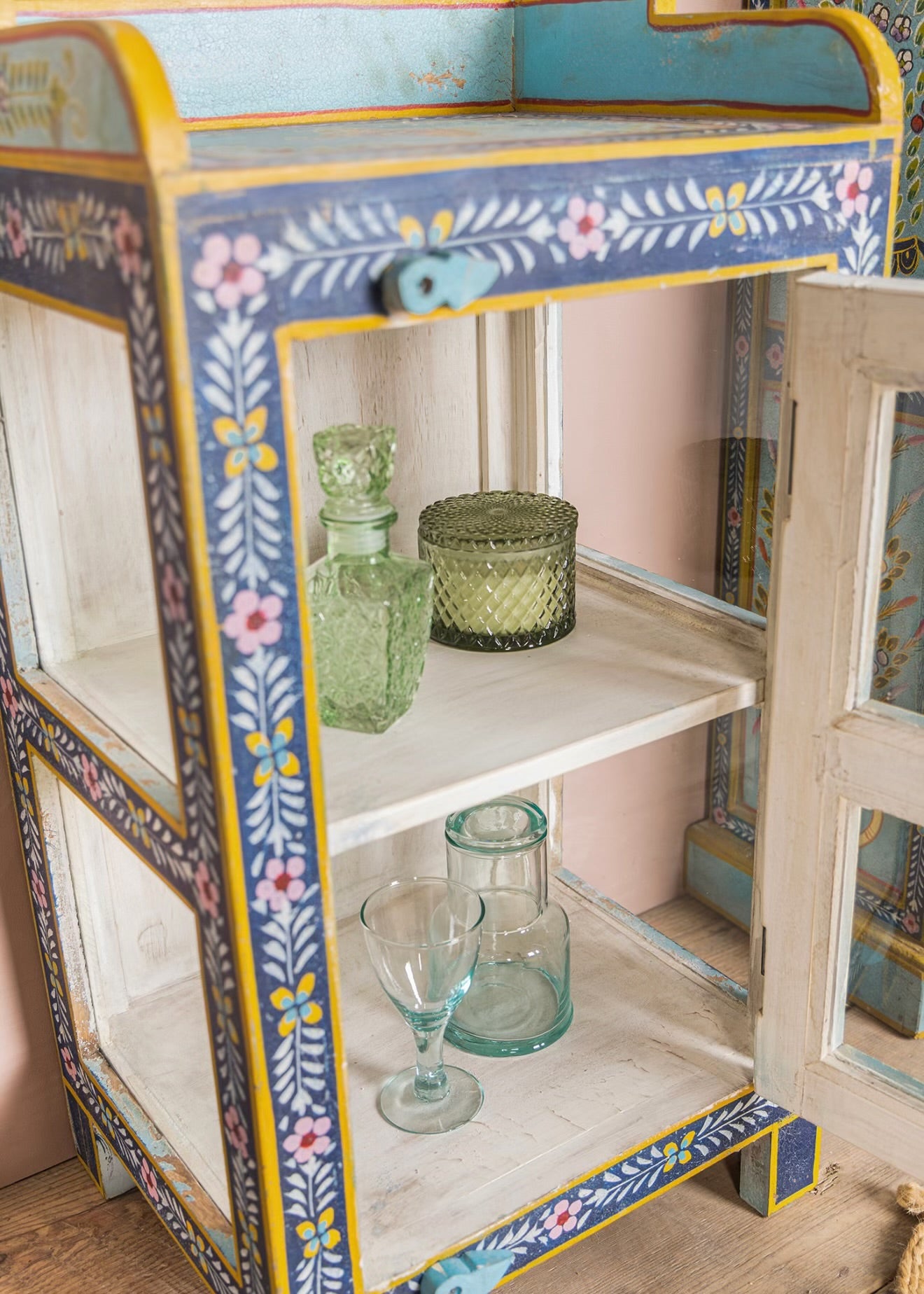 Side view of The Neelam glass display cabinet with hand-painted floral frame and shelving